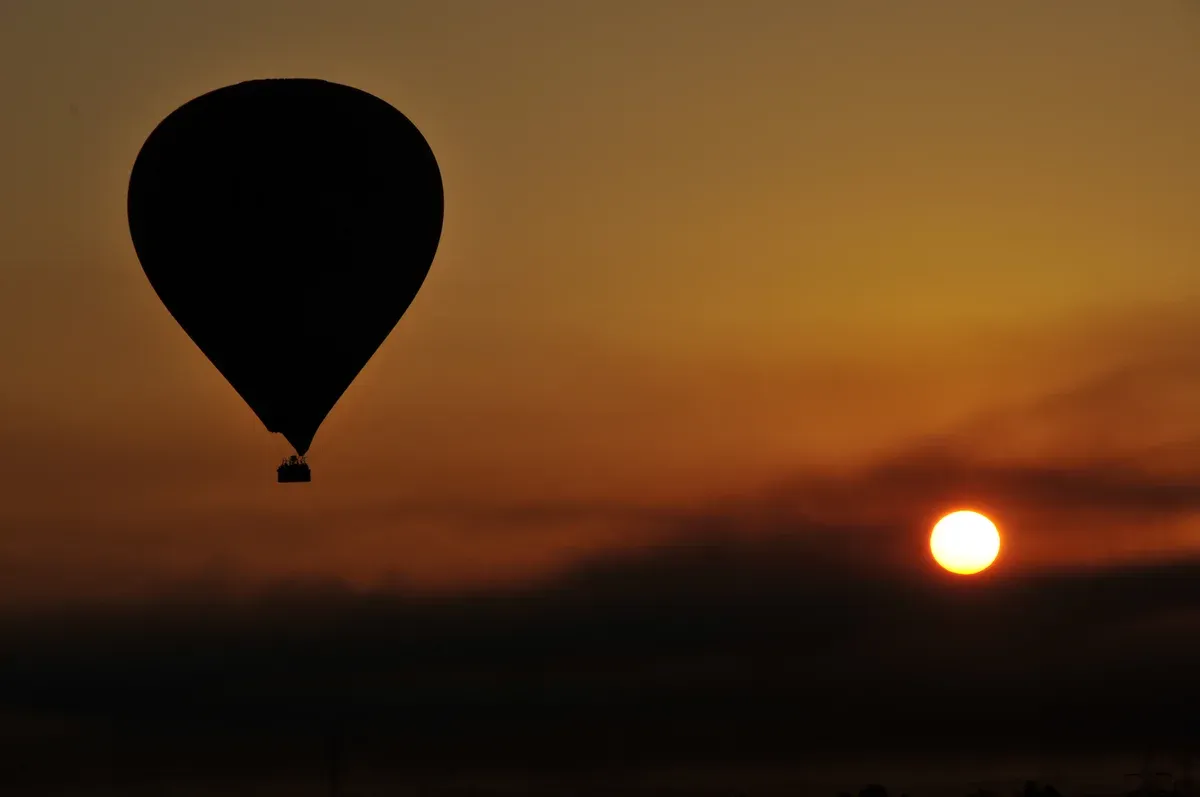 A hot air balloon silhouetted against the rising sun over Luxor, seen on a Valley of the Kings tour